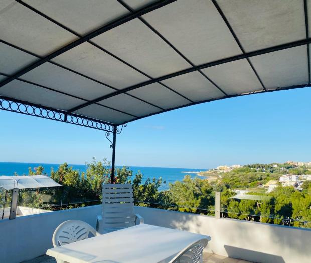 Terrazza con vista mare e colline, cielo sereno.