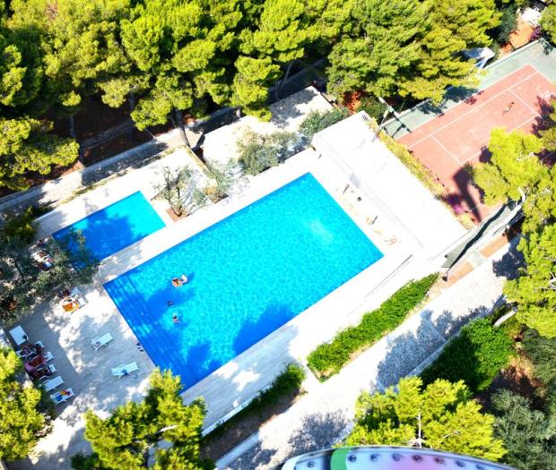 Vista aerea di una piscina e campo da tennis circondati da alberi.