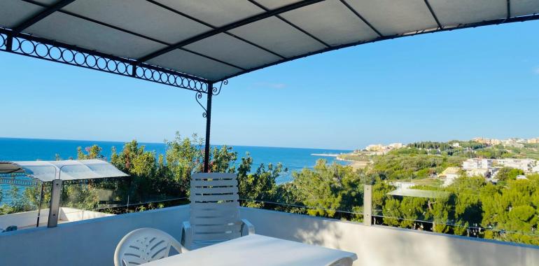 Terrazza con vista mare e colline, cielo sereno.